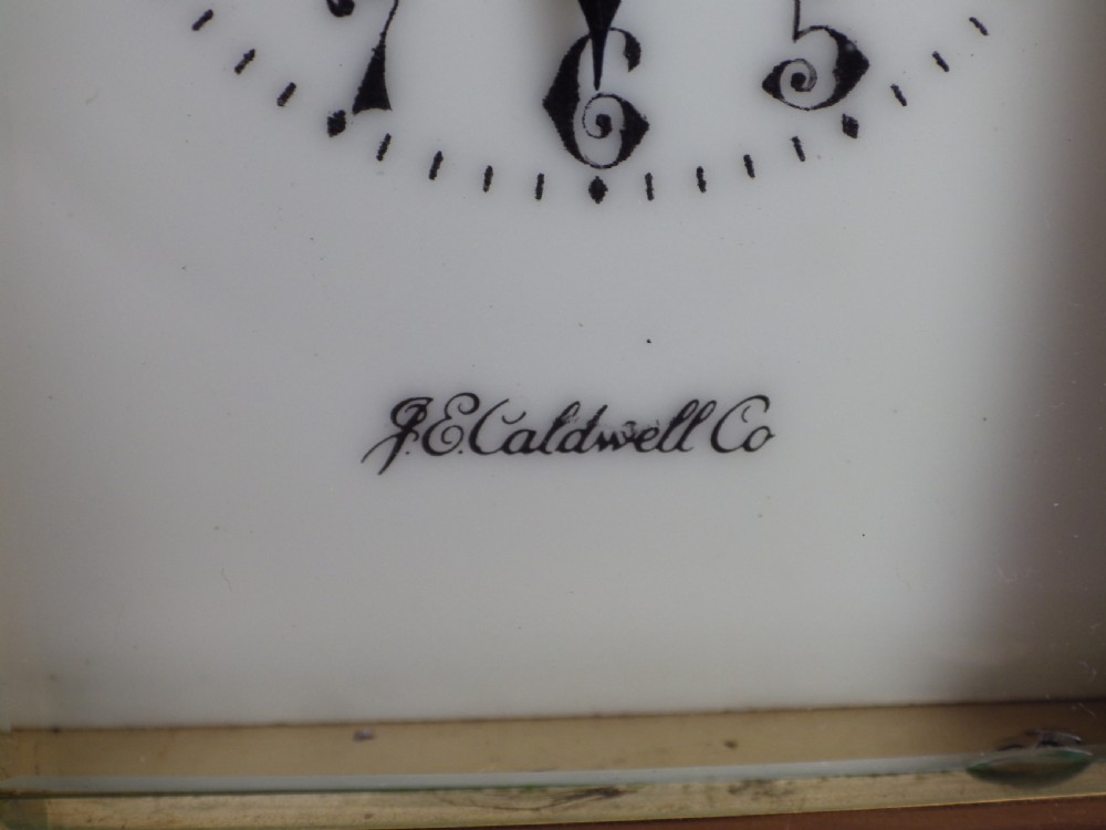 A brass French carriage clock featuring clear glass side panels, a white enamel dial with black numerals, and a hinged brass carrying handle. View VIII