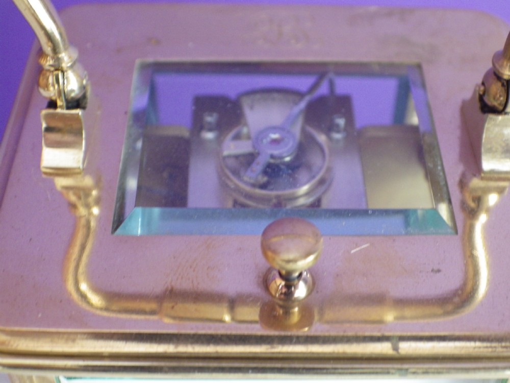 A brass French carriage clock featuring clear glass side panels, a white enamel dial with black numerals, and a hinged brass carrying handle. View IX