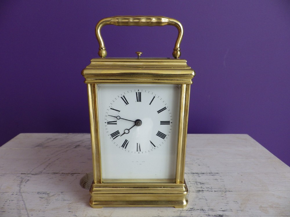 A restored 19th-century French brass gorge case carriage clock featuring a white enamel dial with Roman numerals and a curved carrying handle.