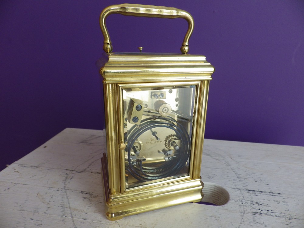 A restored 19th-century French brass gorge case carriage clock featuring a white enamel dial with Roman numerals and a curved carrying handle. View III