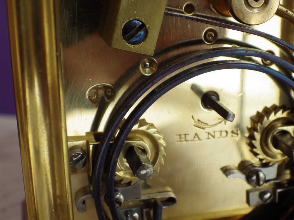 A restored 19th-century French brass gorge case carriage clock featuring a white enamel dial with Roman numerals and a curved carrying handle. View IV