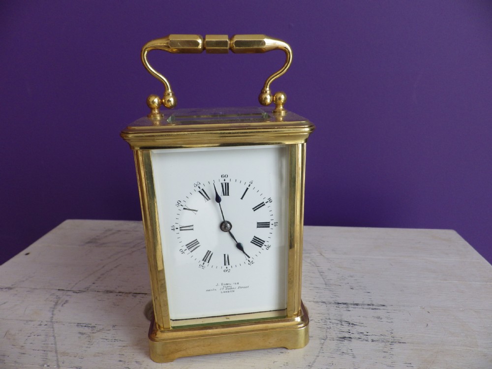 An antique French carriage clock featuring a gilded brass case with clear glass panels, a carrying handle, and a white enamel dial with black Roman numerals.