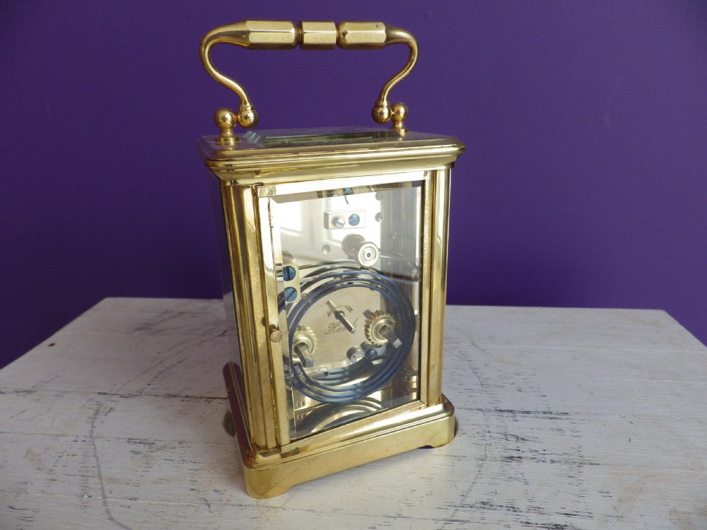 An antique French carriage clock featuring a gilded brass case with clear glass panels, a carrying handle, and a white enamel dial with black Roman numerals. View III