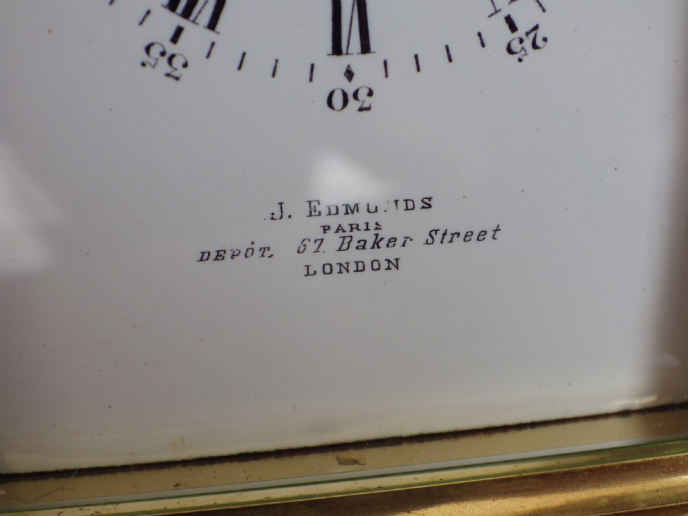 An antique French carriage clock featuring a gilded brass case with clear glass panels, a carrying handle, and a white enamel dial with black Roman numerals. View VI