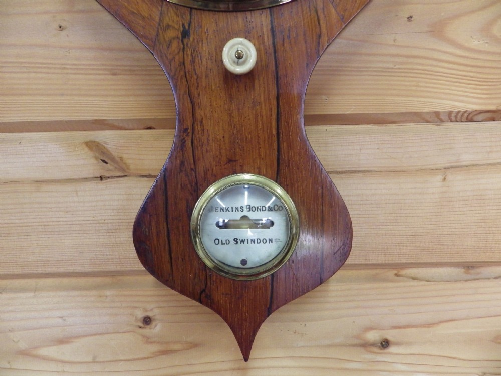 A Victorian wall-mounted mahogany banjo mercury barometer featuring a silvered dial, spirit thermometer, convex mirror, and brass fittings. View II