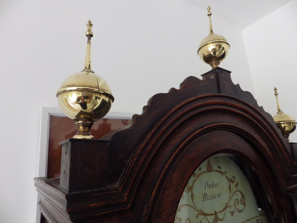 A dark brown Georgian longcase clock featuring three brass finials atop a broken arch pediment and a painted white arch dial face. View VII