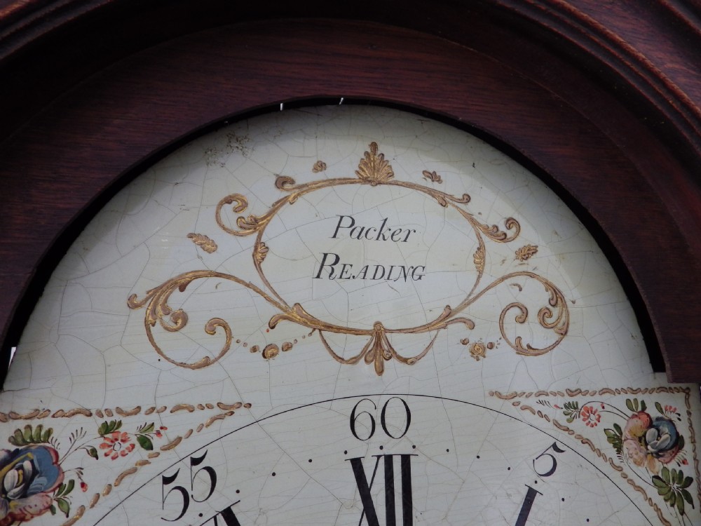 A dark brown Georgian longcase clock featuring three brass finials atop a broken arch pediment and a painted white arch dial face. View VIII