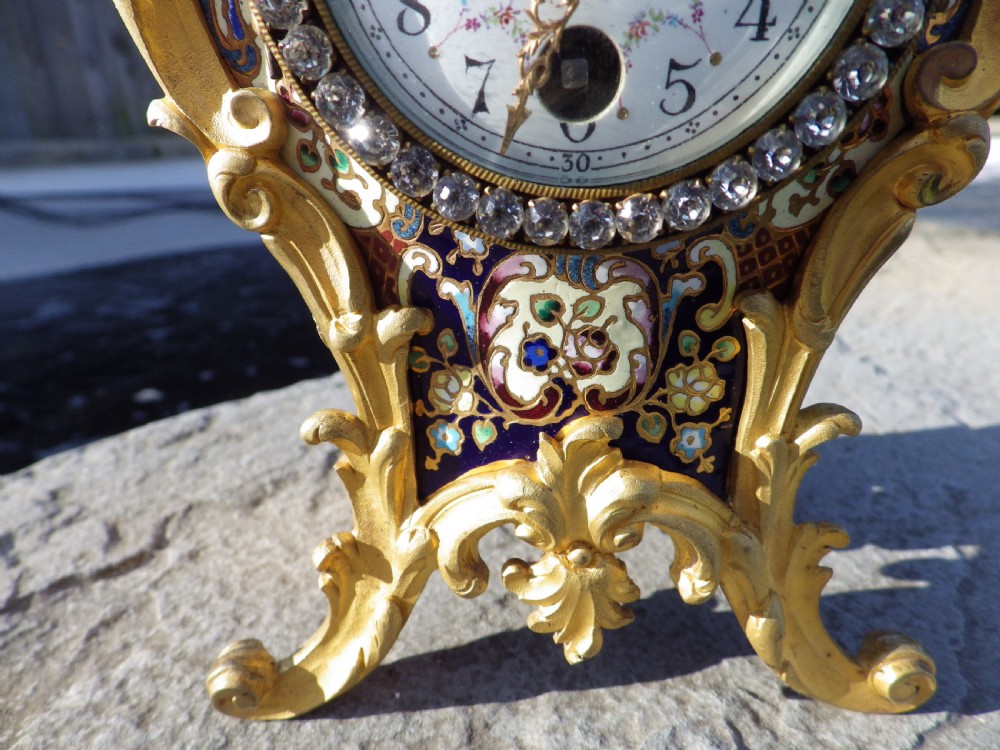 A late 19th-century French Rococo style gilded bronze miniature clock adorned with blue enamel detail and a jewelled crystal bezel surrounding a white dial. View II