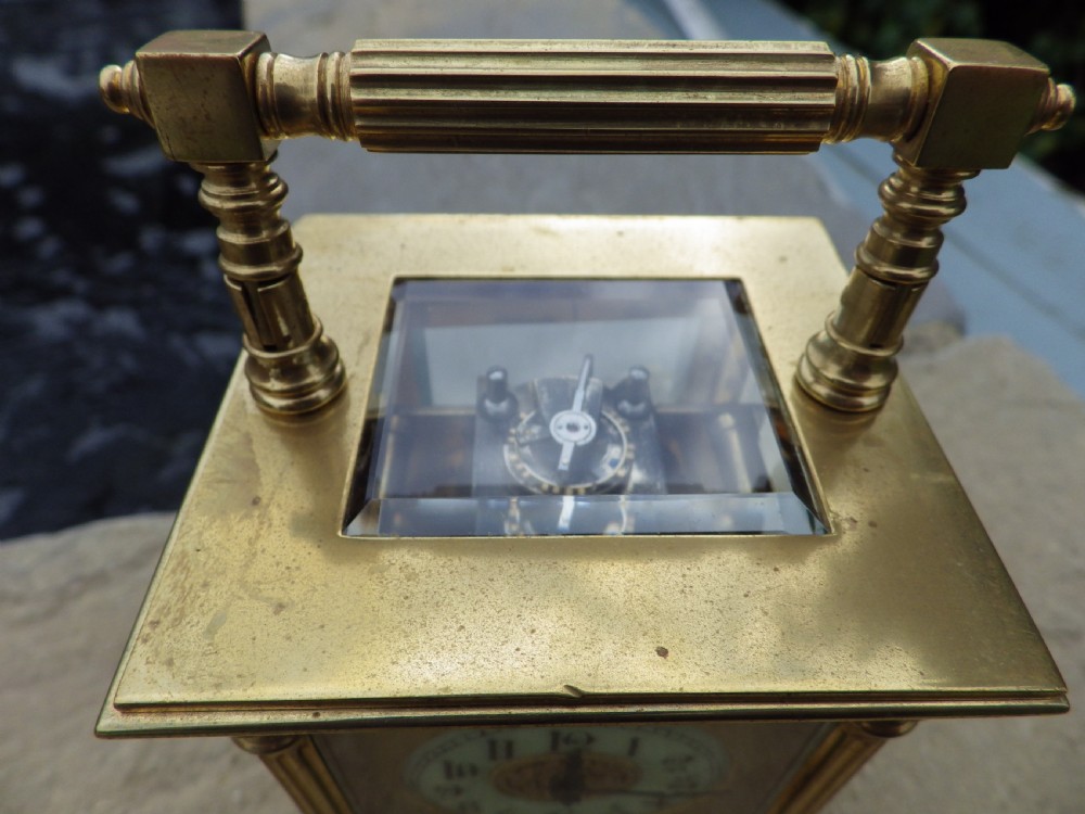 A late nineteenth-century French brass carriage clock featuring an overhead handle, fluted corner columns, an enamel main dial, and a smaller subsidiary alarm dial. View V