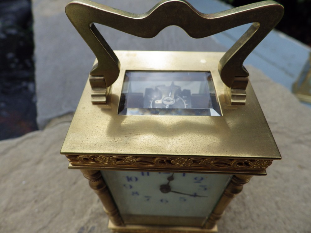 A late 19th-century French brass carriage clock featuring turned corner columns, pierced floral friezes, a white enamel dial with blue numerals, and a hinged top handle. View V