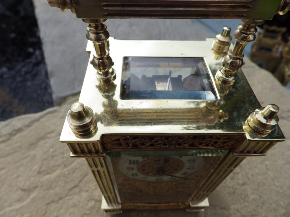An antique French brass carriage clock featuring detailed chased floral fretwork, fluted corner columns, a folding handle, and bevelled glass panels. View V