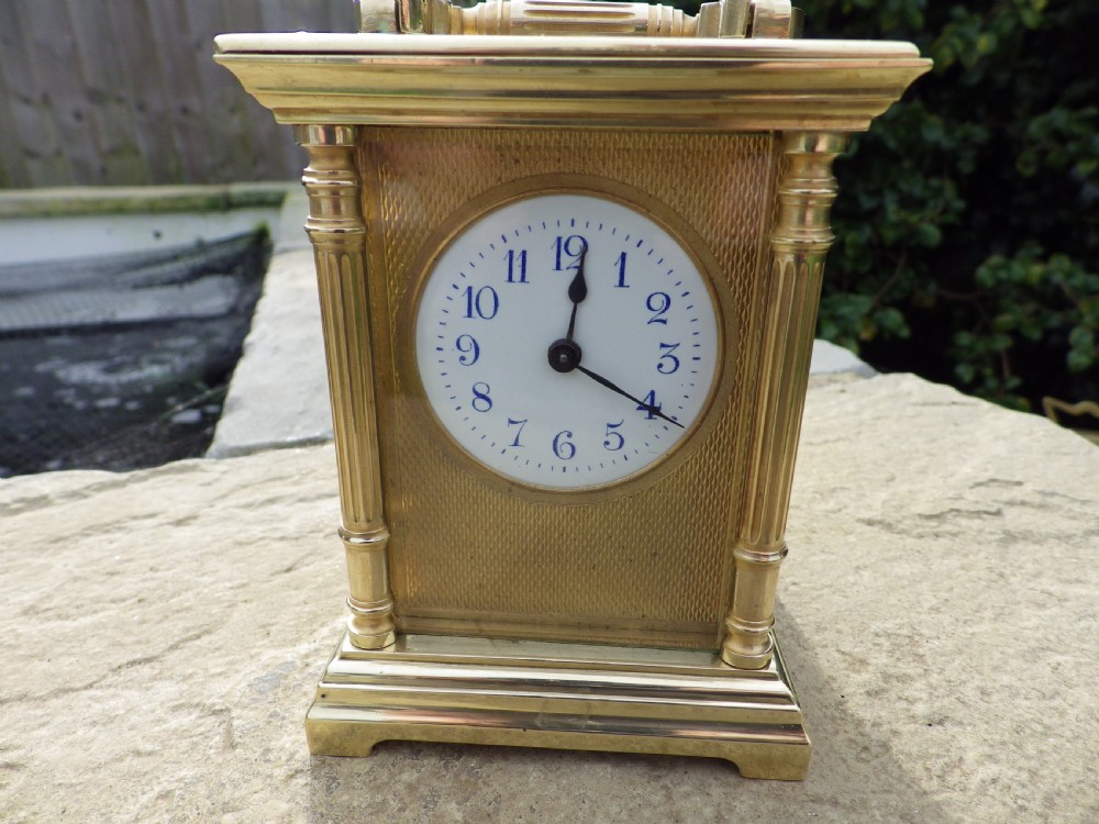A late nineteenth-century French brass carriage clock featuring fluted corner columns, bevelled glass, an engine-turned brass mask, and a white enamel dial. View VI