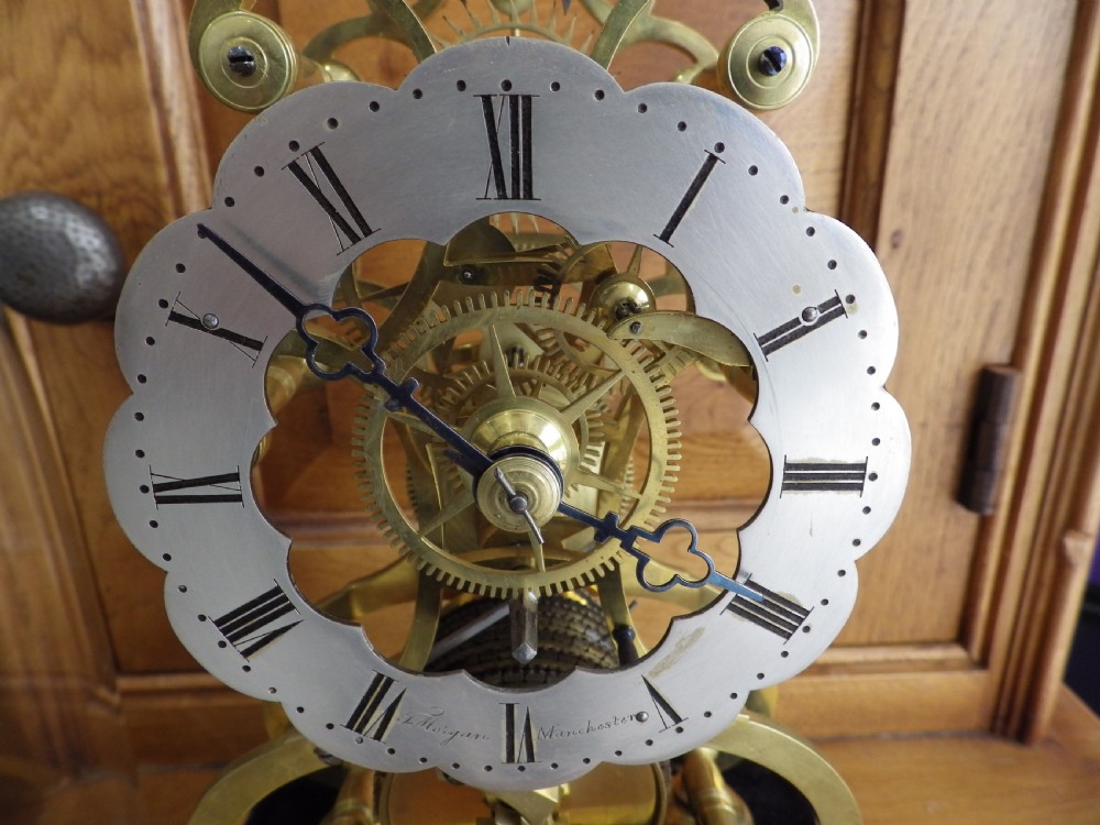An 1870s English brass skeleton clock with an exposed mechanical movement and silvered chapter ring beneath a tall glass dome on a wooden base. View V