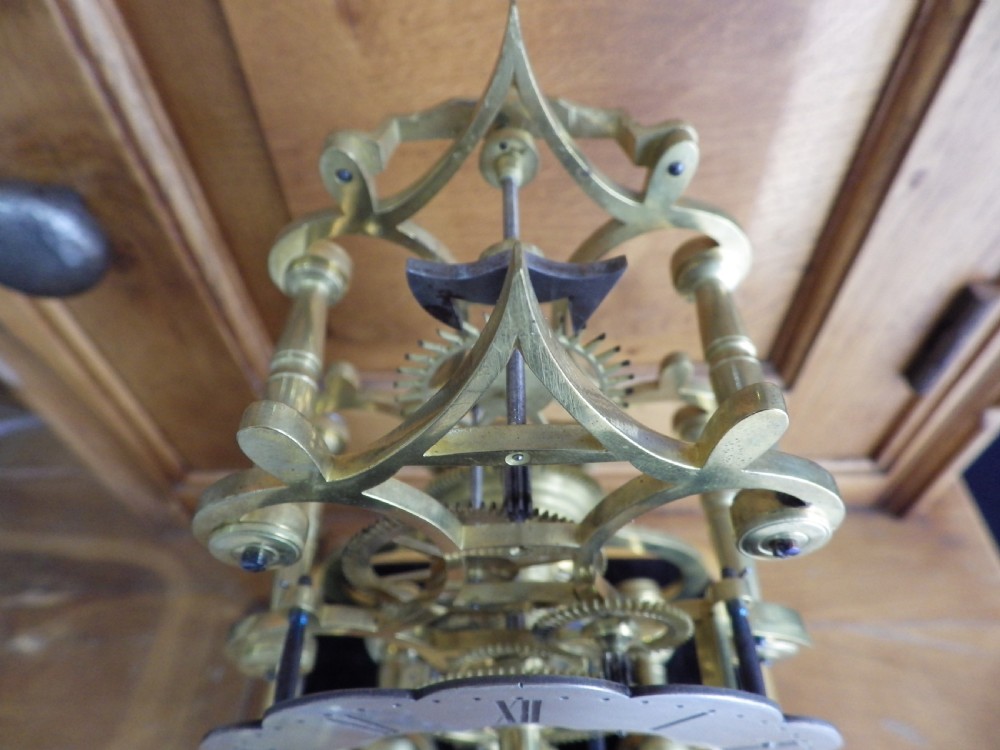 An 1870s English brass skeleton clock with an exposed mechanical movement and silvered chapter ring beneath a tall glass dome on a wooden base. View VI