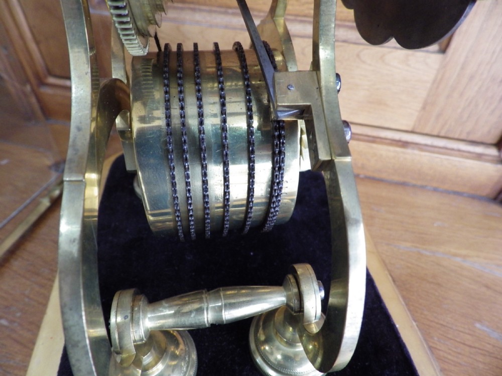 An 1870s English brass skeleton clock with an exposed mechanical movement and silvered chapter ring beneath a tall glass dome on a wooden base. View X