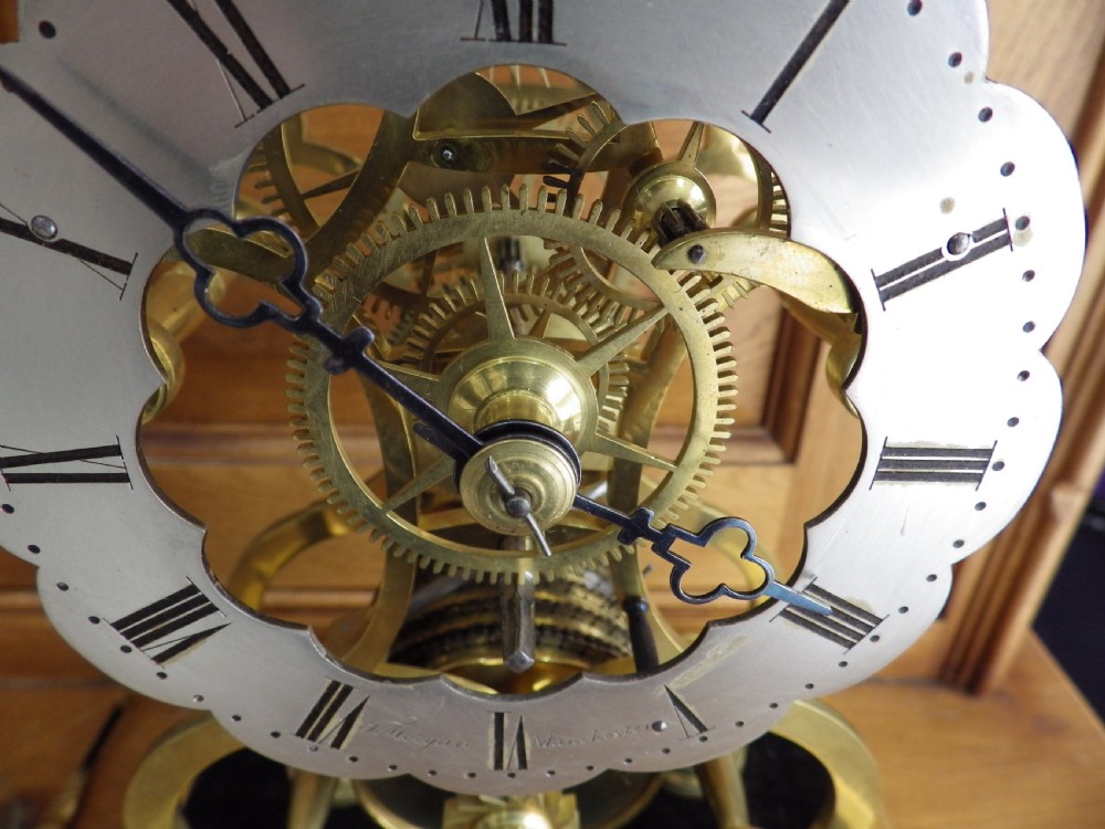 An 1870s English brass skeleton clock with an exposed mechanical movement and silvered chapter ring beneath a tall glass dome on a wooden base. View XI
