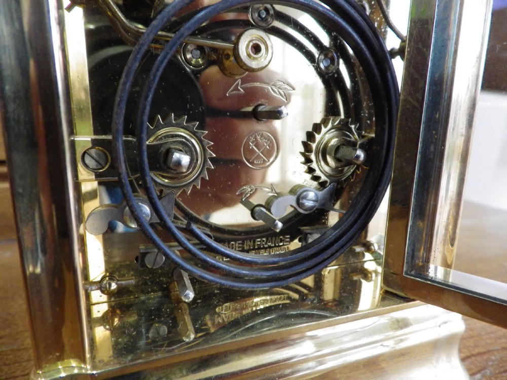 A brass carriage clock with bevelled glass panels, a white enamel dial, three subsidiary dials, and a top carrying handle resting on a dark box. View VI