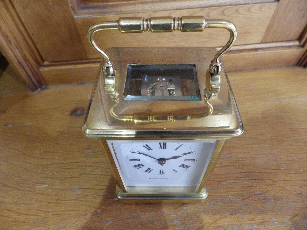 A rectangular Victorian brass carriage clock featuring a top carrying handle, glass side panels, and a white dial with black Roman numerals signed Mappin & Webb Ltd. View V