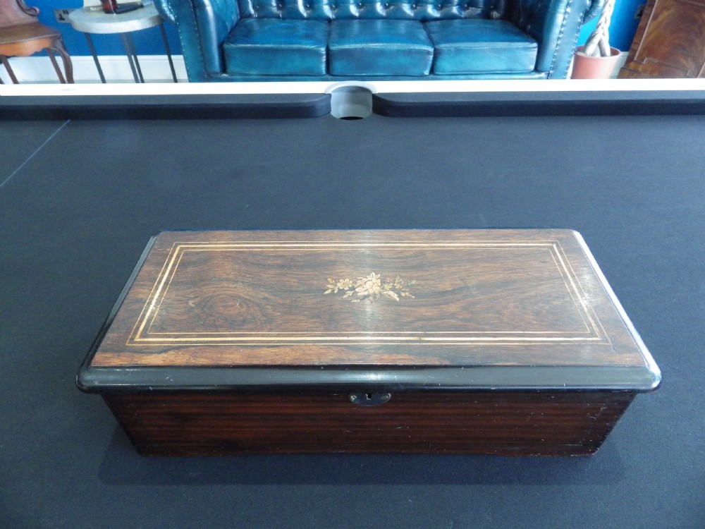 A rectangular dark wood antique music box with a floral marquetry inlay on the lid framed by boxwood stringing.