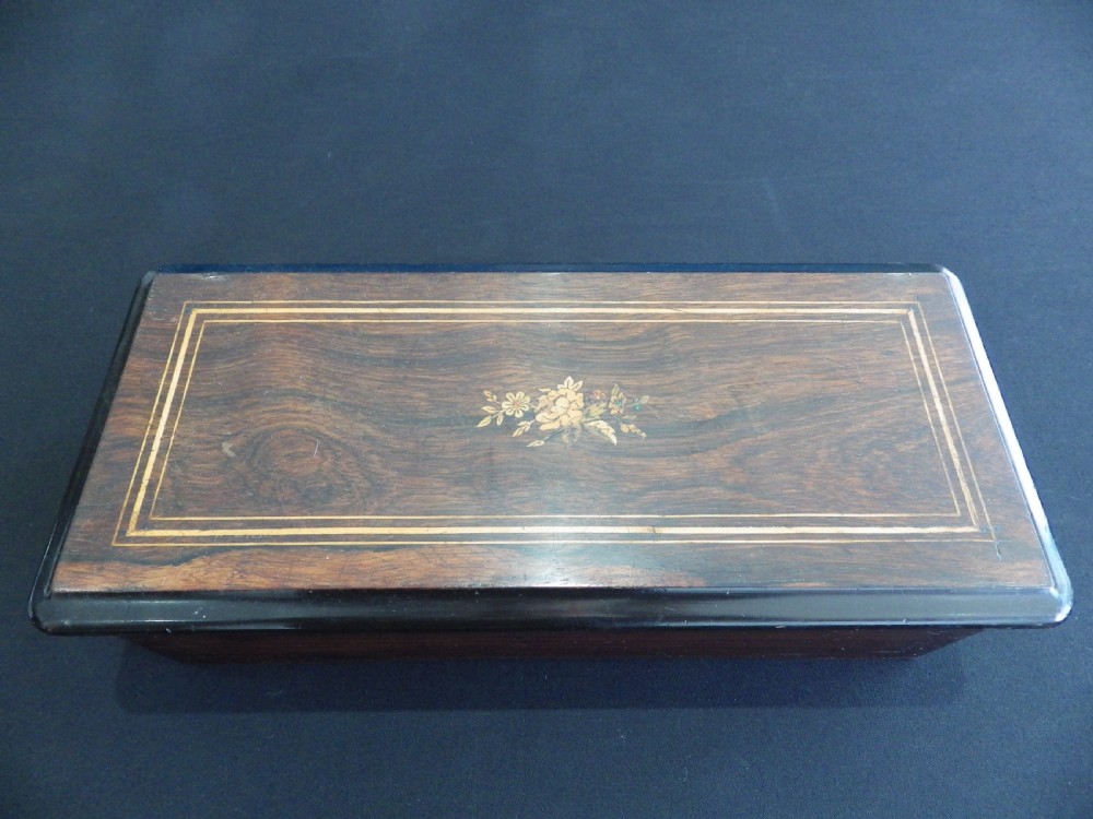 A rectangular dark wood antique music box with a floral marquetry inlay on the lid framed by boxwood stringing. View II