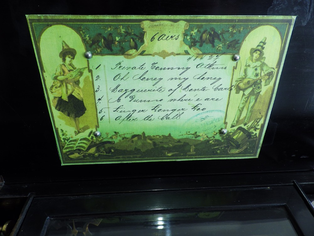 A rectangular dark wood antique music box with a floral marquetry inlay on the lid framed by boxwood stringing. View III