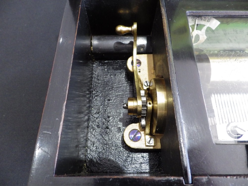 A rectangular dark wood antique music box with a floral marquetry inlay on the lid framed by boxwood stringing. View V