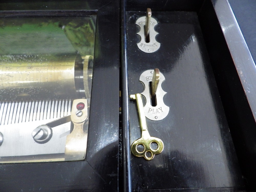 A rectangular dark wood antique music box with a floral marquetry inlay on the lid framed by boxwood stringing. View VI