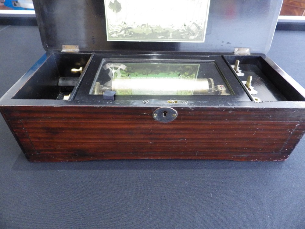 A rectangular dark wood antique music box with a floral marquetry inlay on the lid framed by boxwood stringing. View VII