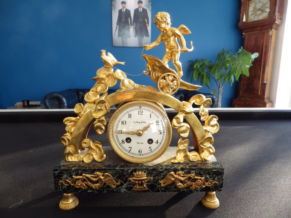 A 19th-century French gilt bronze mantel clock featuring a cherub in a chariot above a white enamel dial, set upon a dark green marble base.