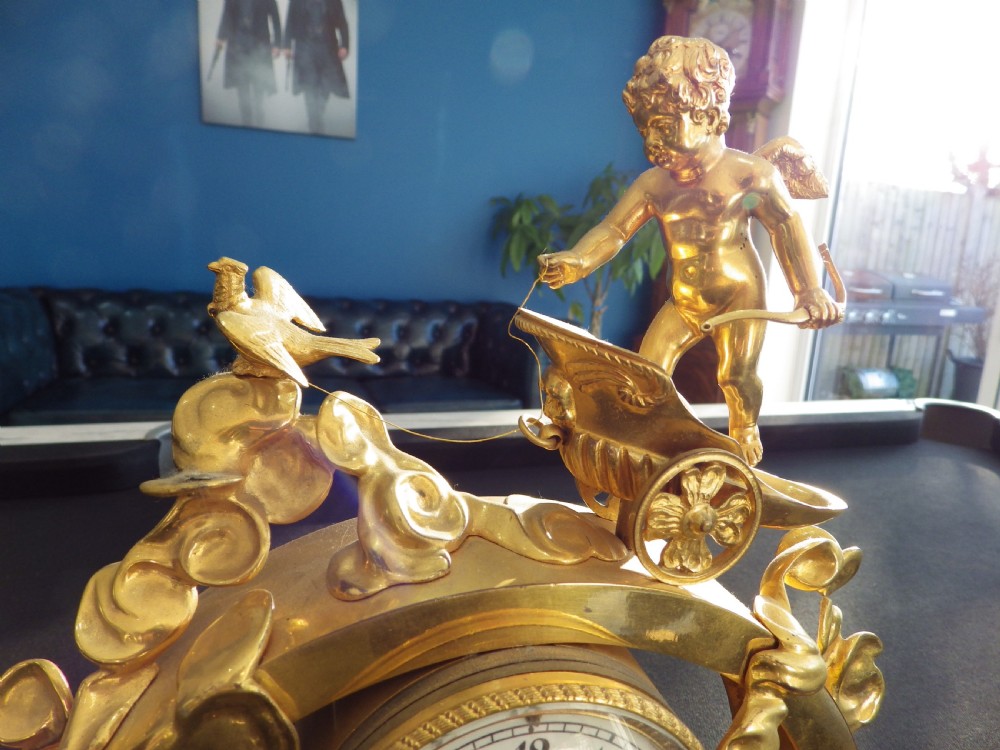 A 19th-century French gilt bronze mantel clock featuring a cherub in a chariot above a white enamel dial, set upon a dark green marble base. View II