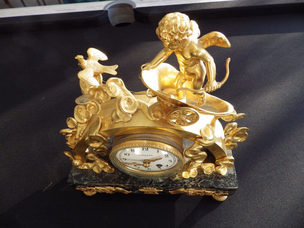 A 19th-century French gilt bronze mantel clock featuring a cherub in a chariot above a white enamel dial, set upon a dark green marble base. View III