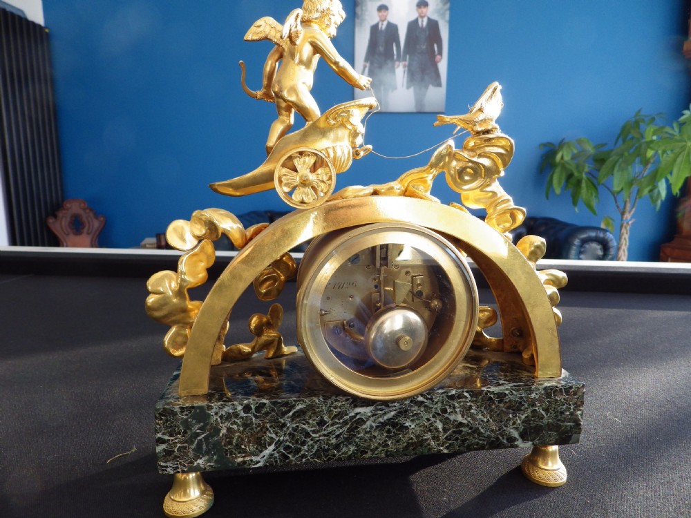 A 19th-century French gilt bronze mantel clock featuring a cherub in a chariot above a white enamel dial, set upon a dark green marble base. View IV
