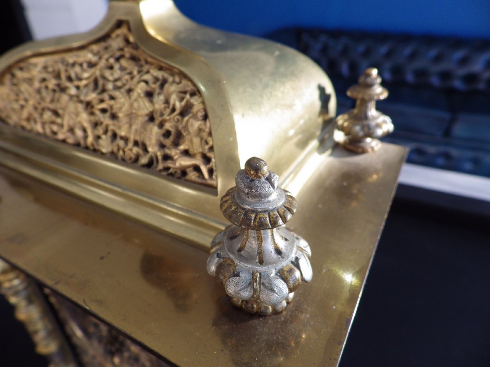 An 1870s French solid brass mantel clock featuring ornate filigree, corner columns, a finial cresting, and a Roman numeral dial. View VII