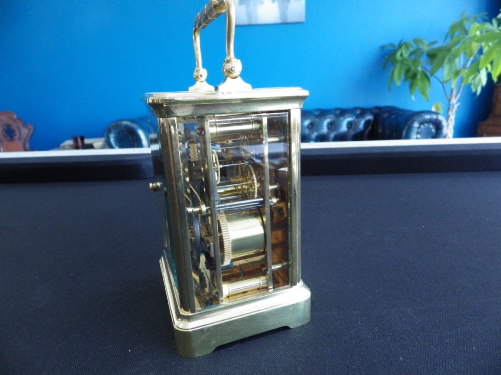 A late 19th-century French brass carriage clock featuring glass side panels, a top carrying handle, and a white enamel dial with black Roman numerals. View V