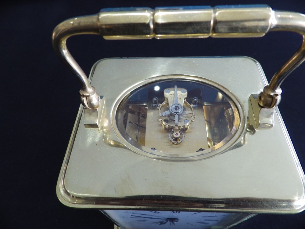 A late 19th-century French brass carriage clock featuring glass side panels, a top carrying handle, and a white enamel dial with black Roman numerals. View VI