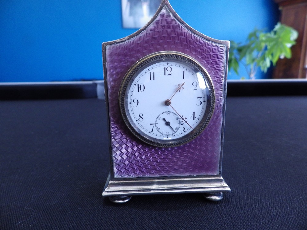 A French miniature silver travel clock featuring purple guilloche enamel, a white enamel dial with Arabic numerals, and ball feet.