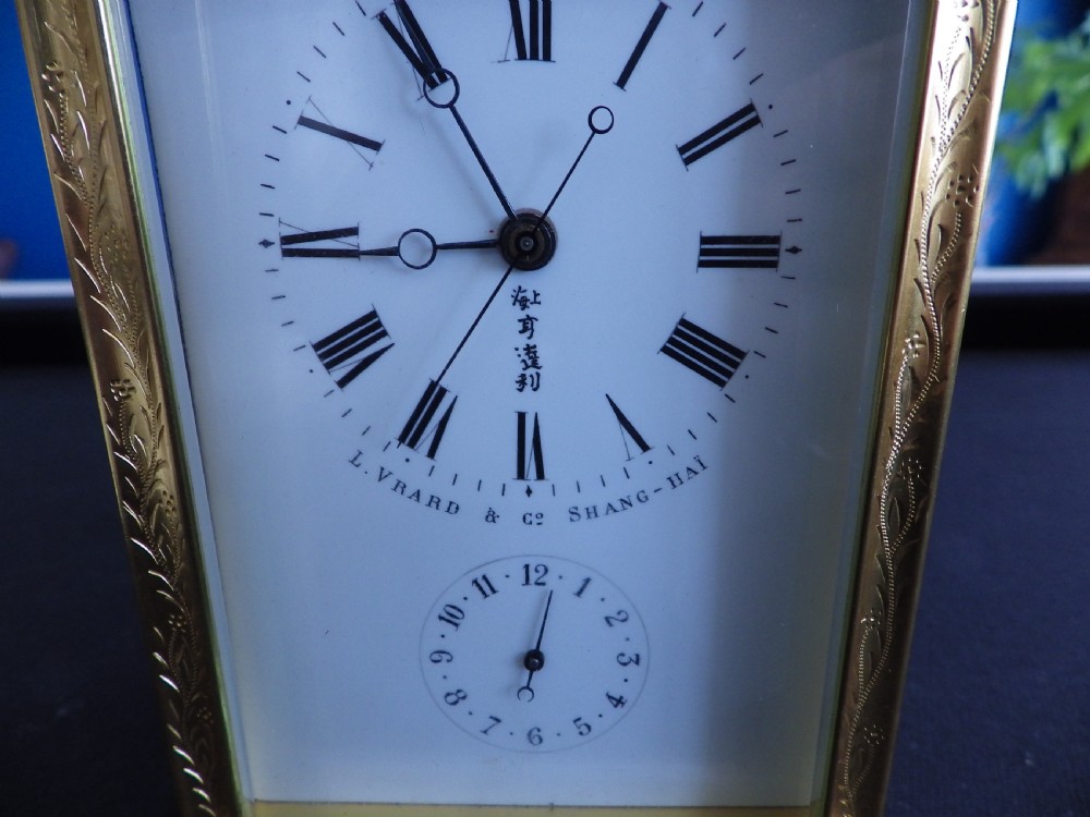 An engraved gilded brass carriage clock featuring a white enamel dial with Roman numerals, a sub-dial, Chinese inscriptions, and a hinged top handle. View II