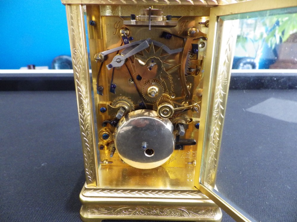 An engraved gilded brass carriage clock featuring a white enamel dial with Roman numerals, a sub-dial, Chinese inscriptions, and a hinged top handle. View V