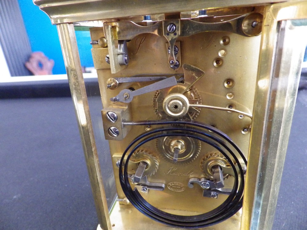 A rectangular antique brass French carriage clock featuring bevelled glass side panels, a top carrying handle, and a white enamelled dial with black Roman numerals. View V