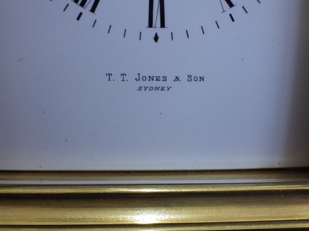 A rectangular antique brass French carriage clock featuring bevelled glass side panels, a top carrying handle, and a white enamelled dial with black Roman numerals. View VII