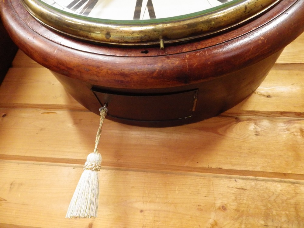 An antique circular mahogany wall clock featuring an eighteen-inch off-white dial with black Roman numerals, black spade hands, and a brass bezel. View II
