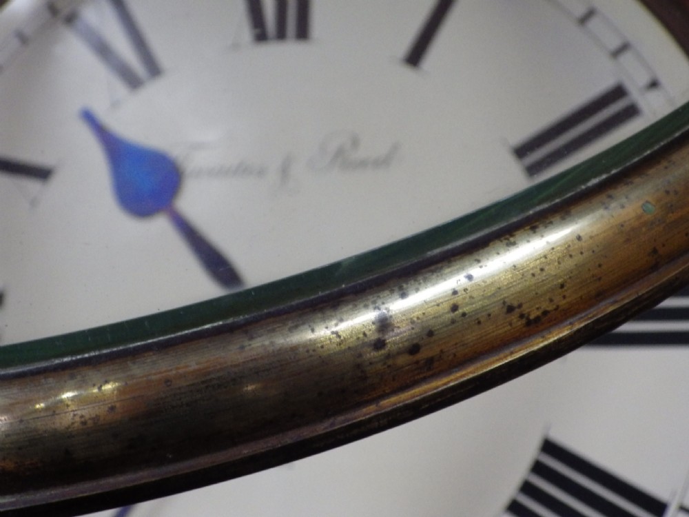 An antique circular mahogany wall clock featuring an eighteen-inch off-white dial with black Roman numerals, black spade hands, and a brass bezel. View VII