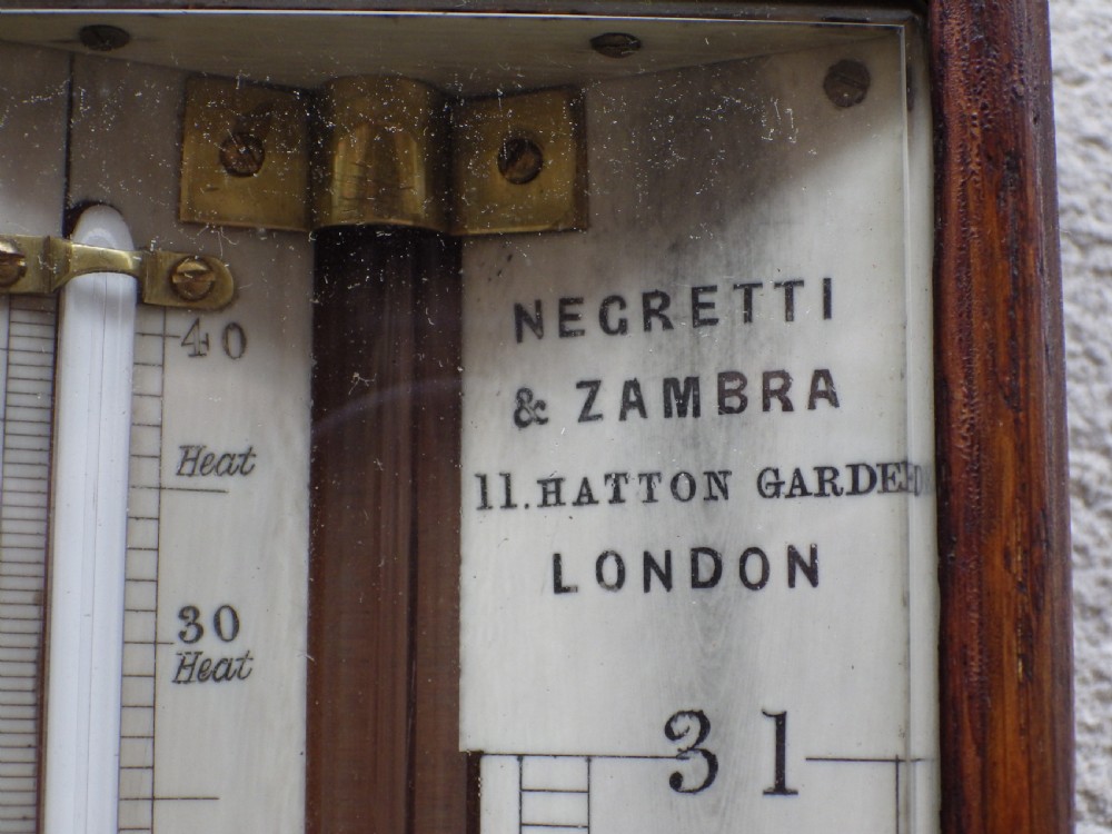 A late Victorian dark oak stick barometer featuring a glass tube weather register behind a glazed door and a carved cylindrical cistern cover at the base. View V