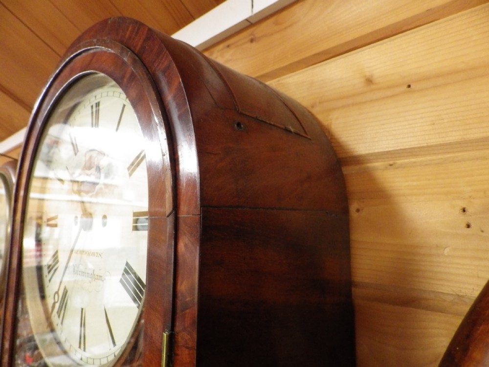 A Victorian flame mahogany wall clock featuring an arched top, painted dial with Roman numerals, carved fretwork, and a glass door displaying a brass pendulum. View V