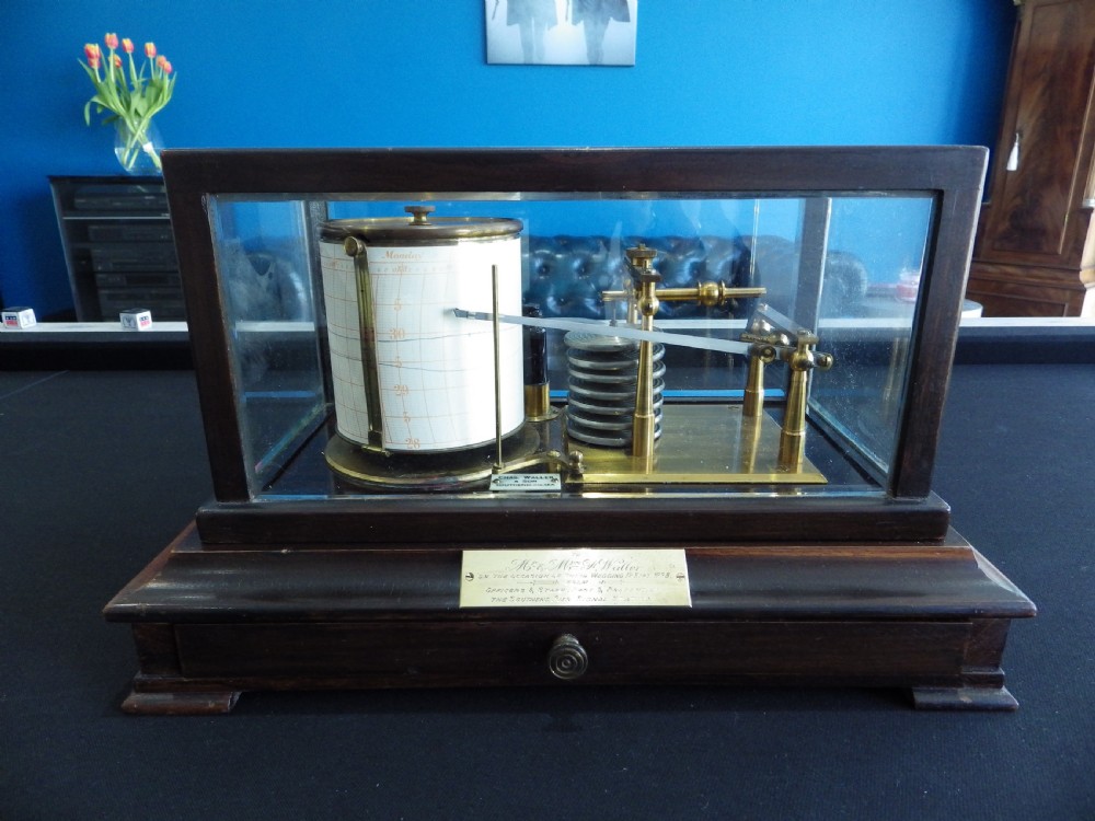 A 1920s mahogany and glass barograph featuring brass internal mechanisms, an aneroid capsule stack, and an engraved brass presentation plaque on the drawer base.
