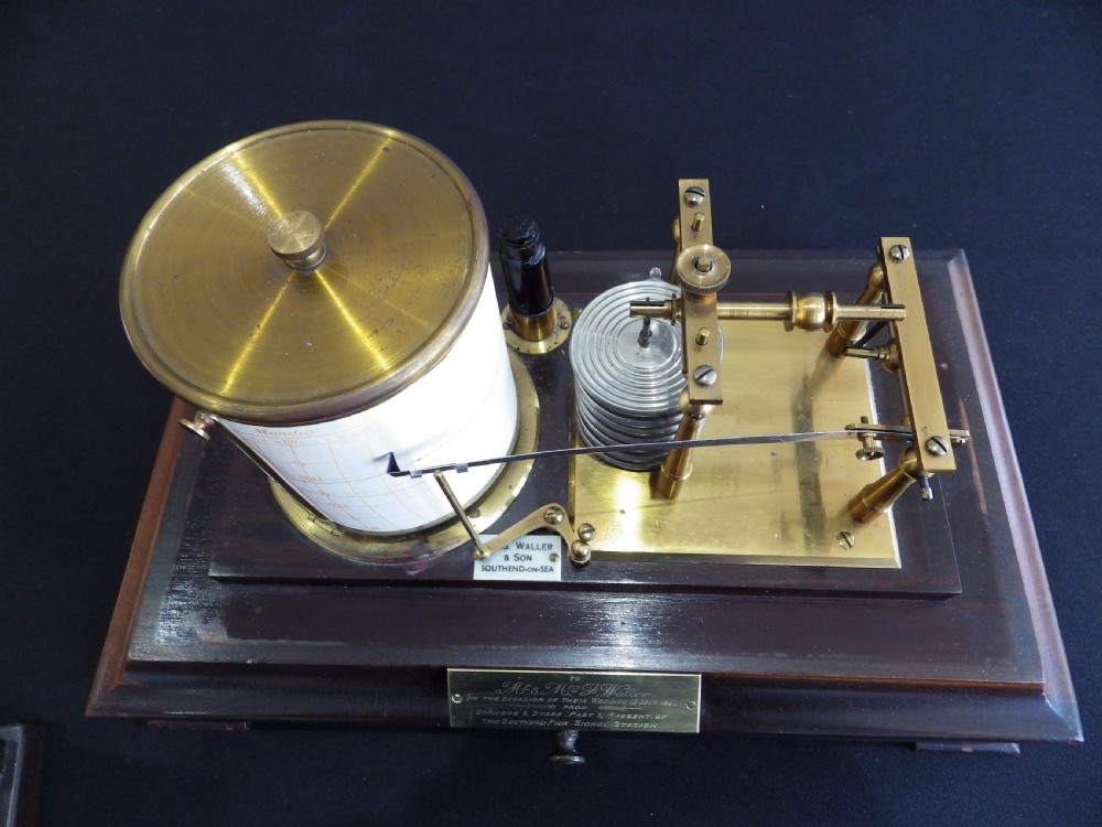 A 1920s mahogany and glass barograph featuring brass internal mechanisms, an aneroid capsule stack, and an engraved brass presentation plaque on the drawer base. View V