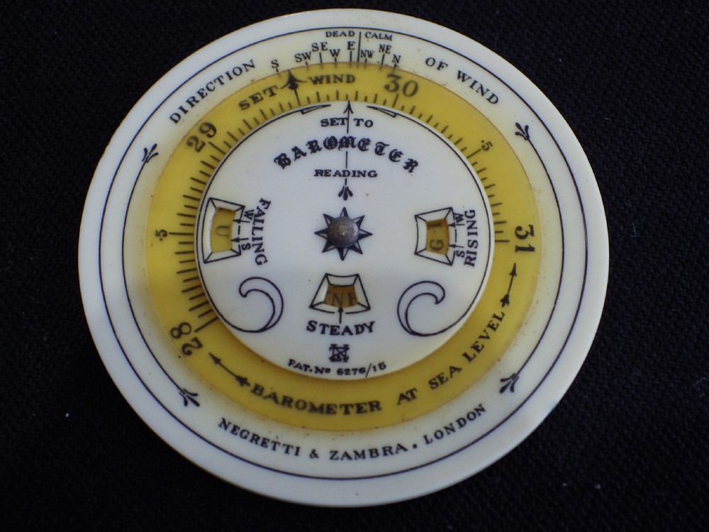An antique circular Negretti and Zambra pocket weather forecaster made from cream and yellow celluloid with printed text dials.