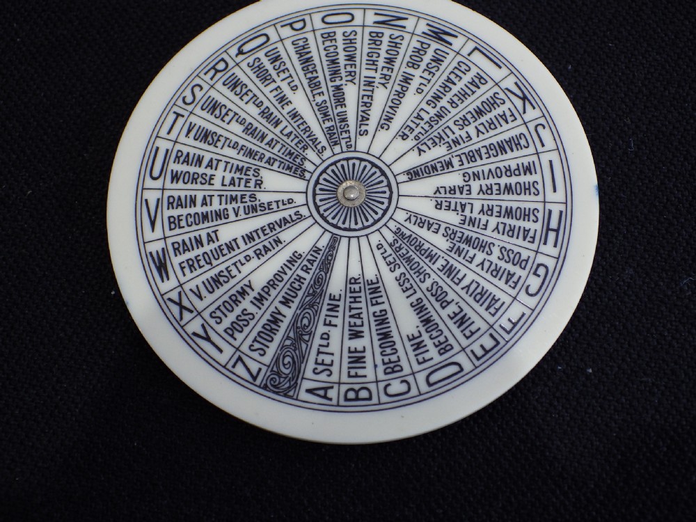 An antique circular Negretti and Zambra pocket weather forecaster made from cream and yellow celluloid with printed text dials. View II