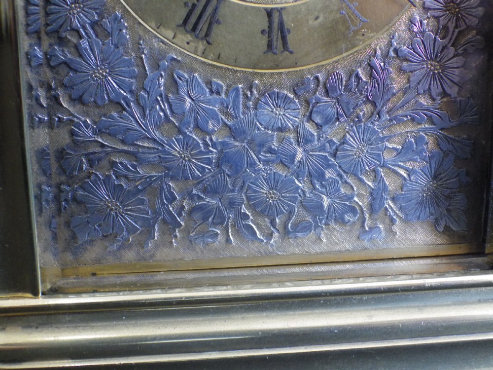 An antique brass carriage clock featuring an ornate silvered floral dial plate, Roman numerals, a top carrying handle, and an accompanying brass winding key. View IV