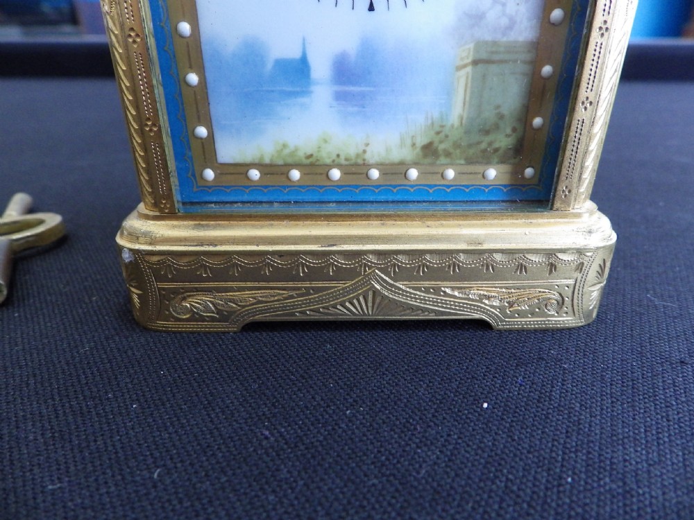 An engraved brass French carriage clock featuring a carrying handle, white enamel Roman numeral dial, and a hand-painted landscape panel. View III